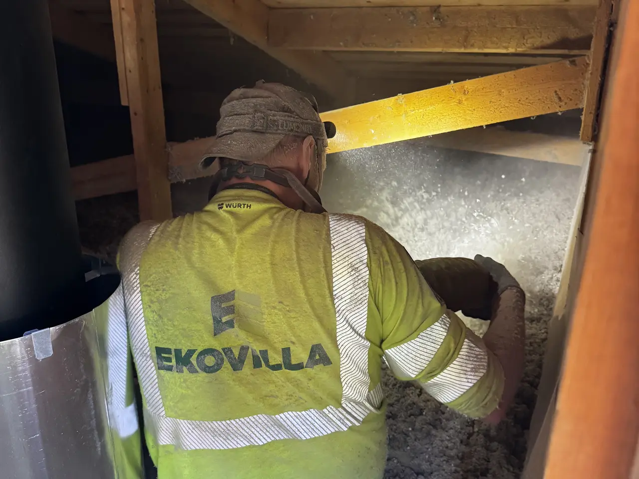 Installatör i Ekovilla-väst vid en vindslucka med isoleringsslang